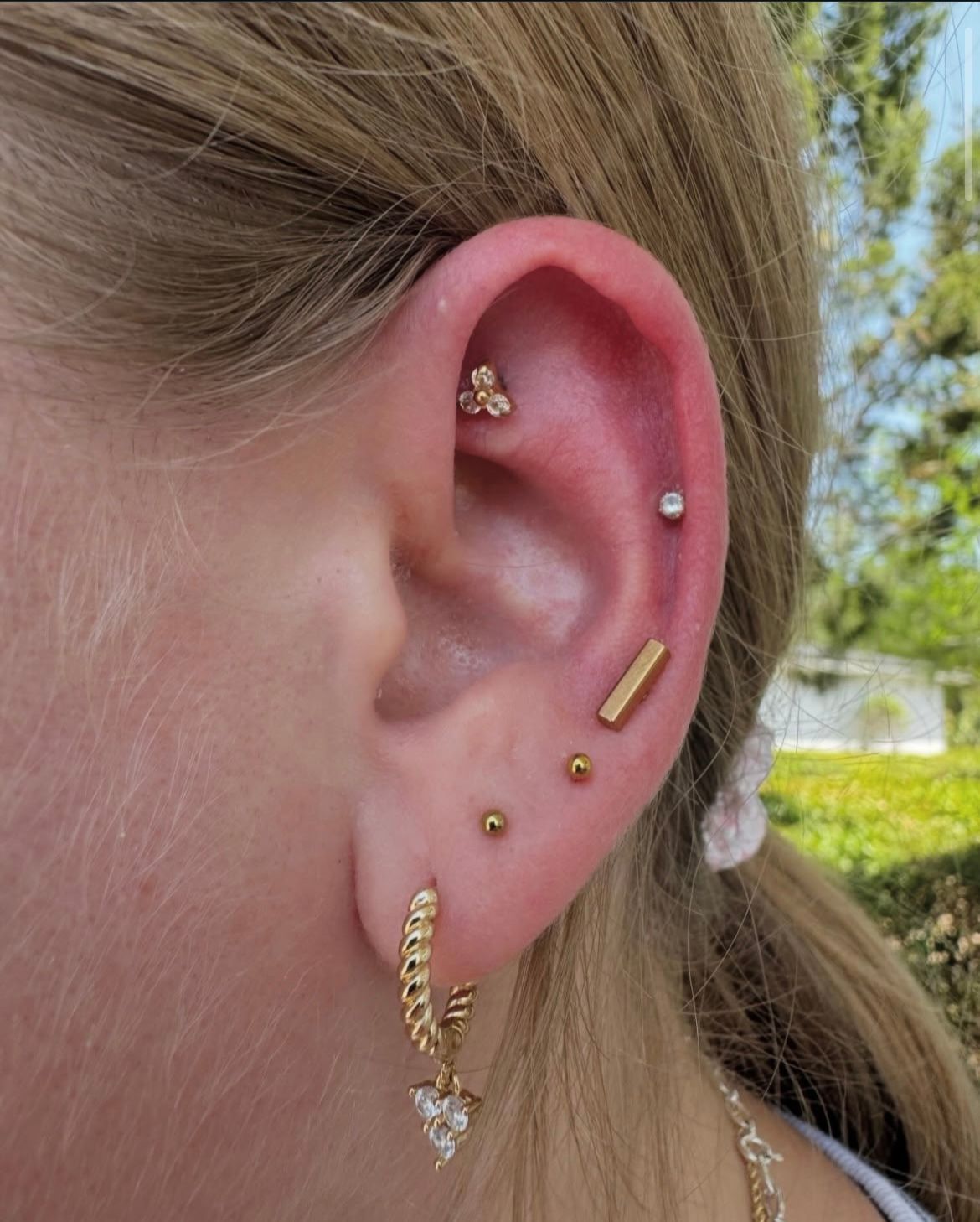 A close-up of an ear with multiple gold piercings, including a helix, tragus, and lobe piercings.