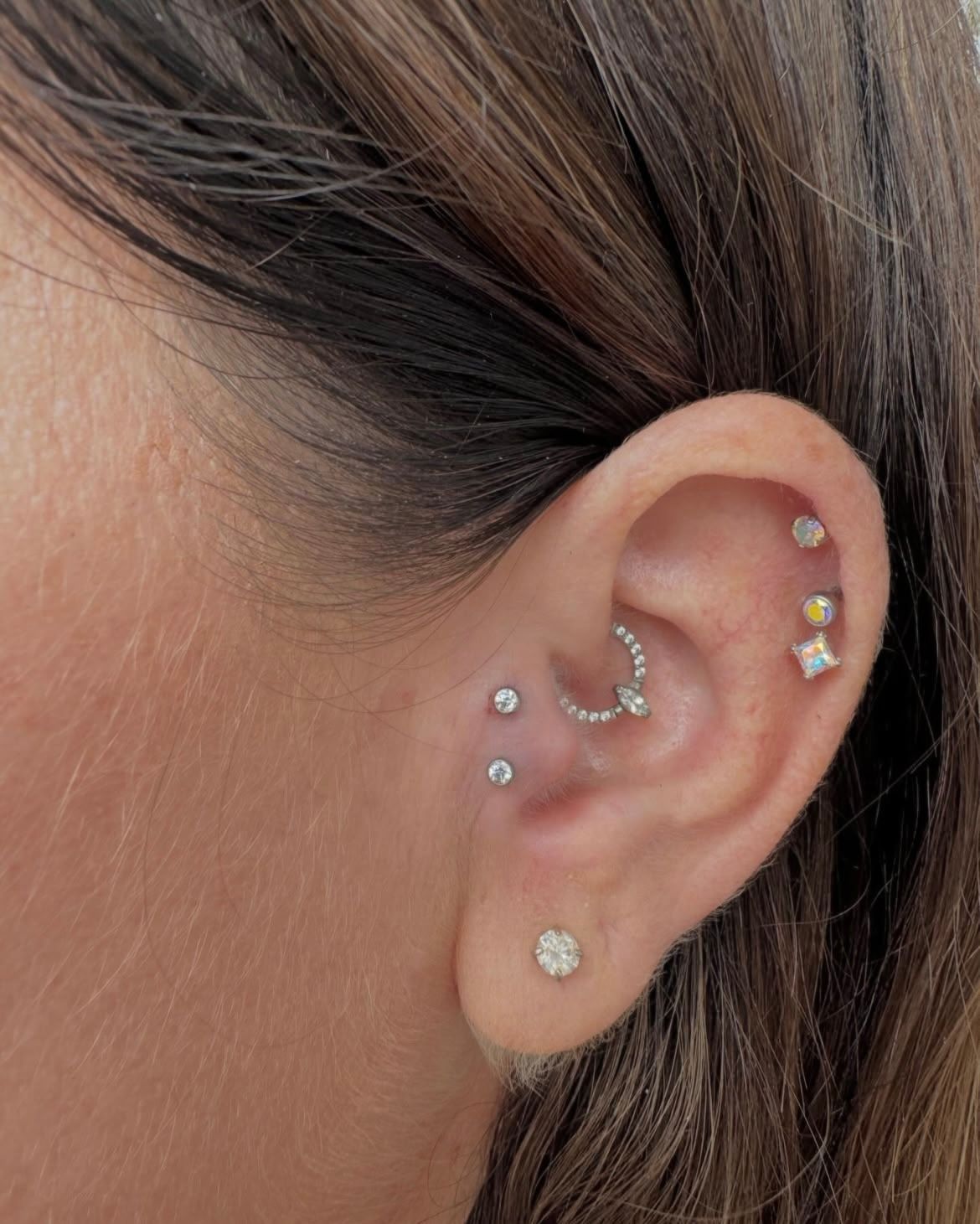 Close-up of a person's ear with multiple ear piercings, including studs and a hoop earring.