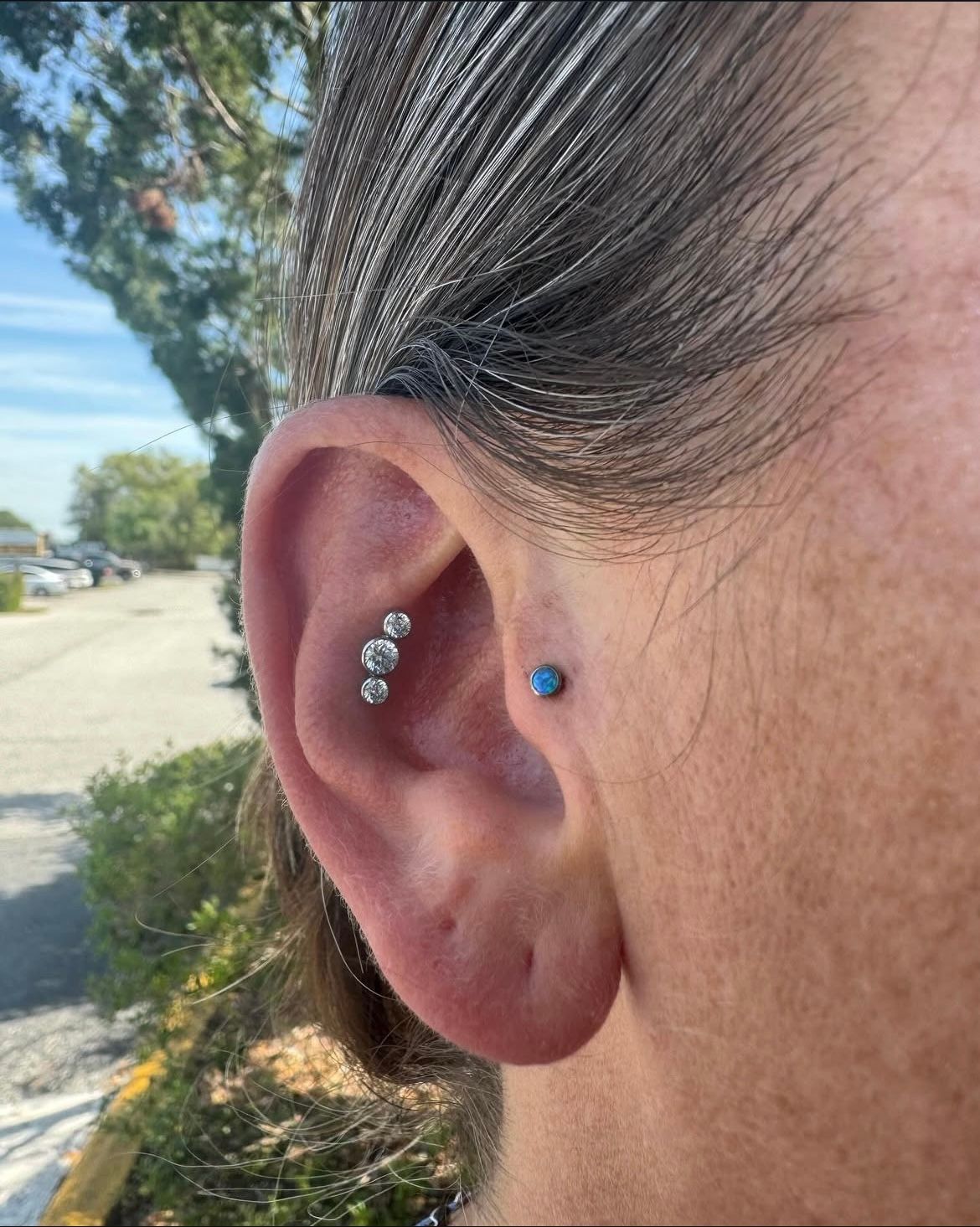 Ear with multiple piercings: three small clear stones in the inner ear, one blue stud on the outer ear.