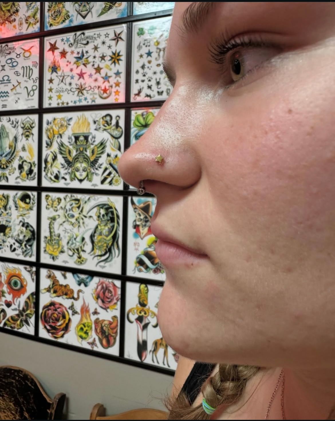 Woman with nose piercing, gazing right, in front of a wall of tattoo flash art.