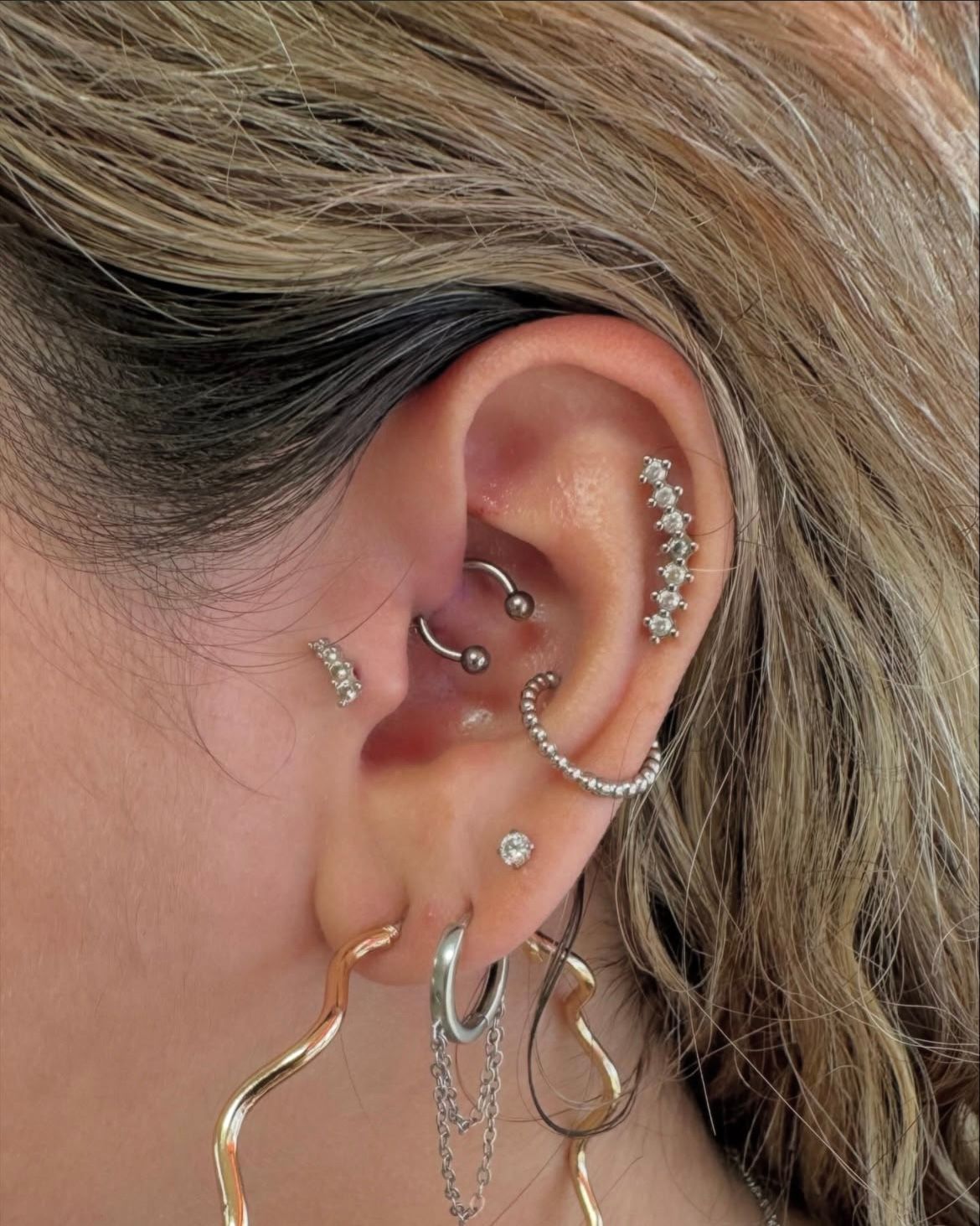 Ear with multiple piercings and various silver jewelry.