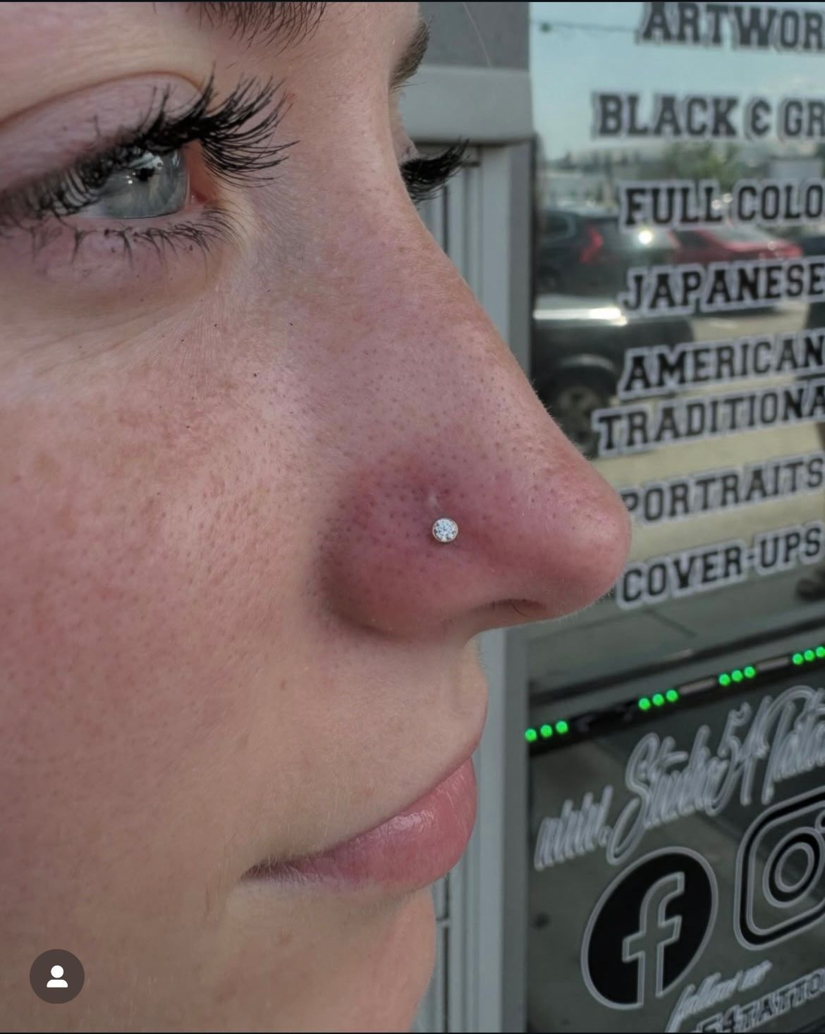 Woman with a nose piercing, a small stud, in front of a tattoo shop.