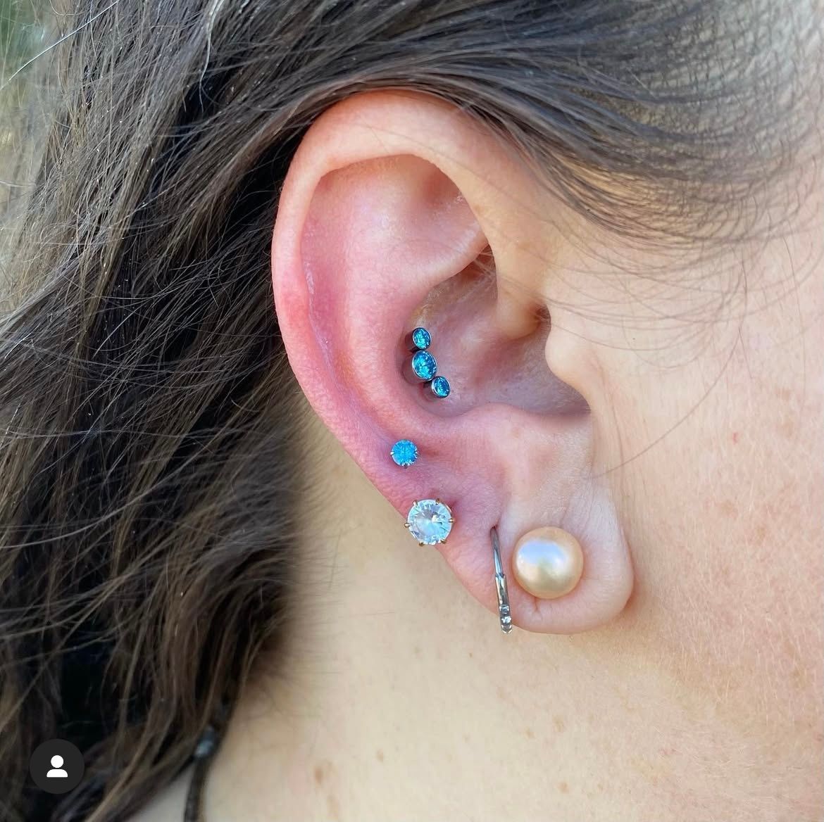 Ear with multiple piercings: helix, tragus, and lobe, featuring turquoise and pearl-toned jewelry.