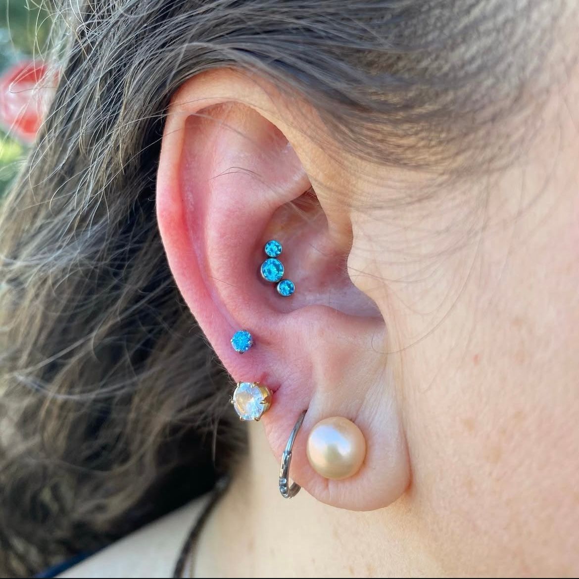 Ear with multiple piercings: turquoise, gold, pearl earrings.