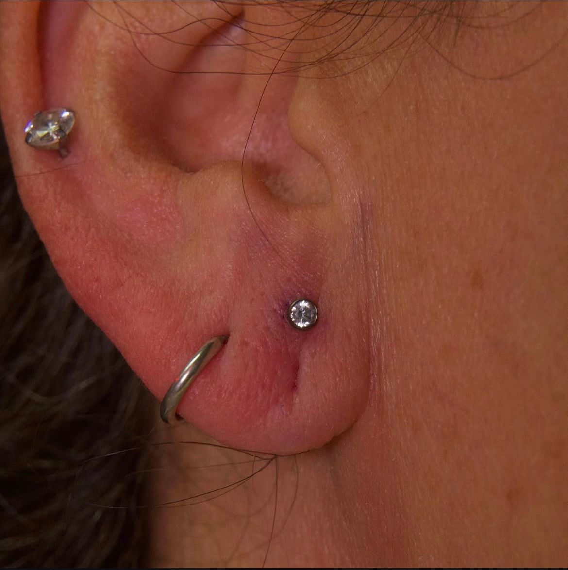 Close-up of a person's ear with three piercings: a stud, a hoop, and another stud.