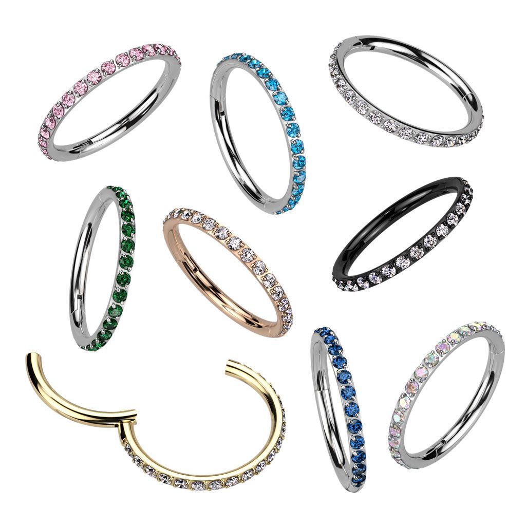 Close-up of multiple rings with colored gems. Pink, blue, green, black, and gold rings in a variety of styles.