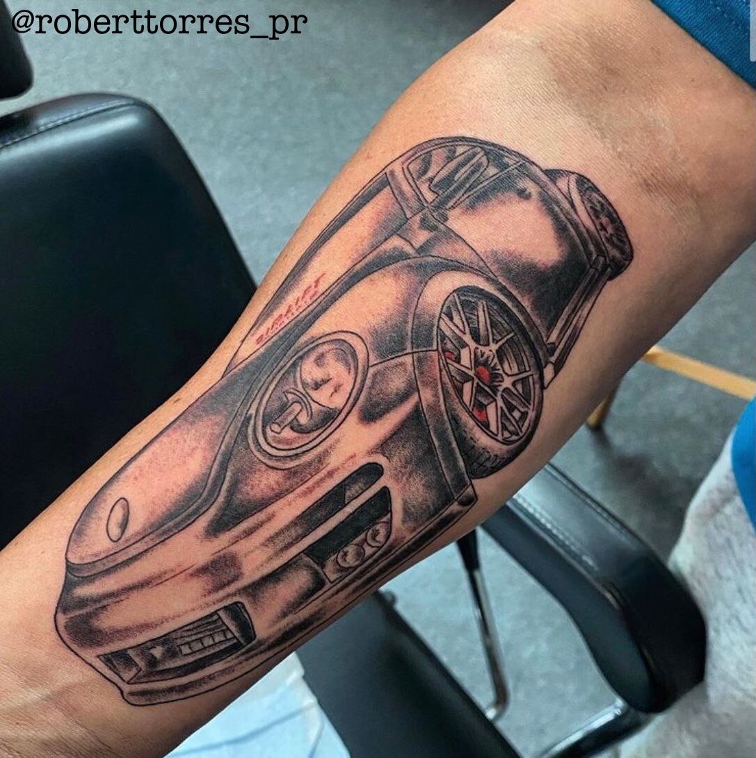 Black and gray car tattoo on a person's forearm, showcasing the vehicle's details and design.
