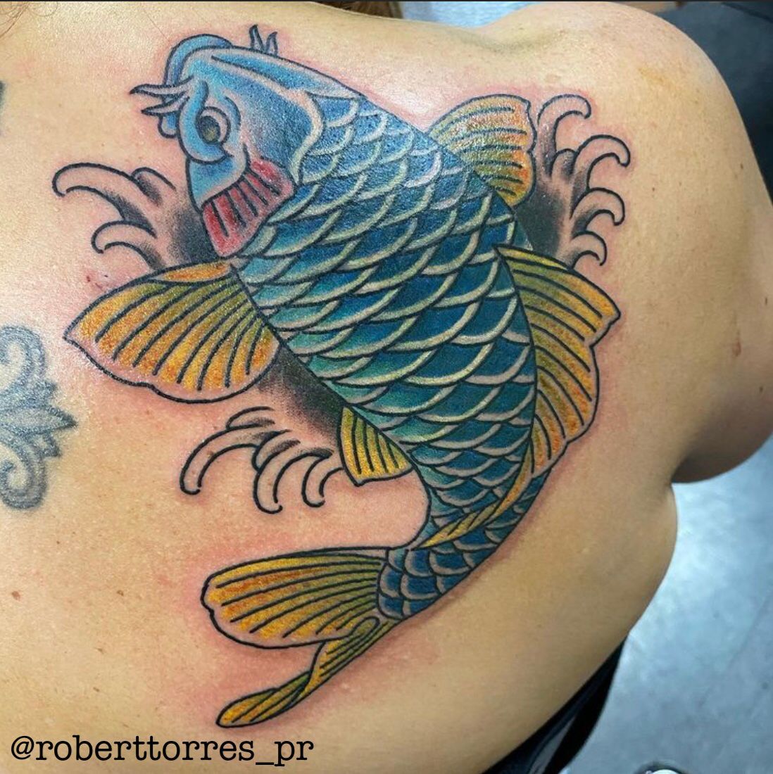 Blue and yellow koi fish tattoo on a person's back.