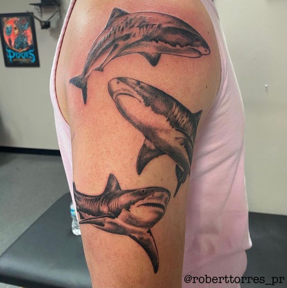 Three black and grey shark tattoos on a person's arm.