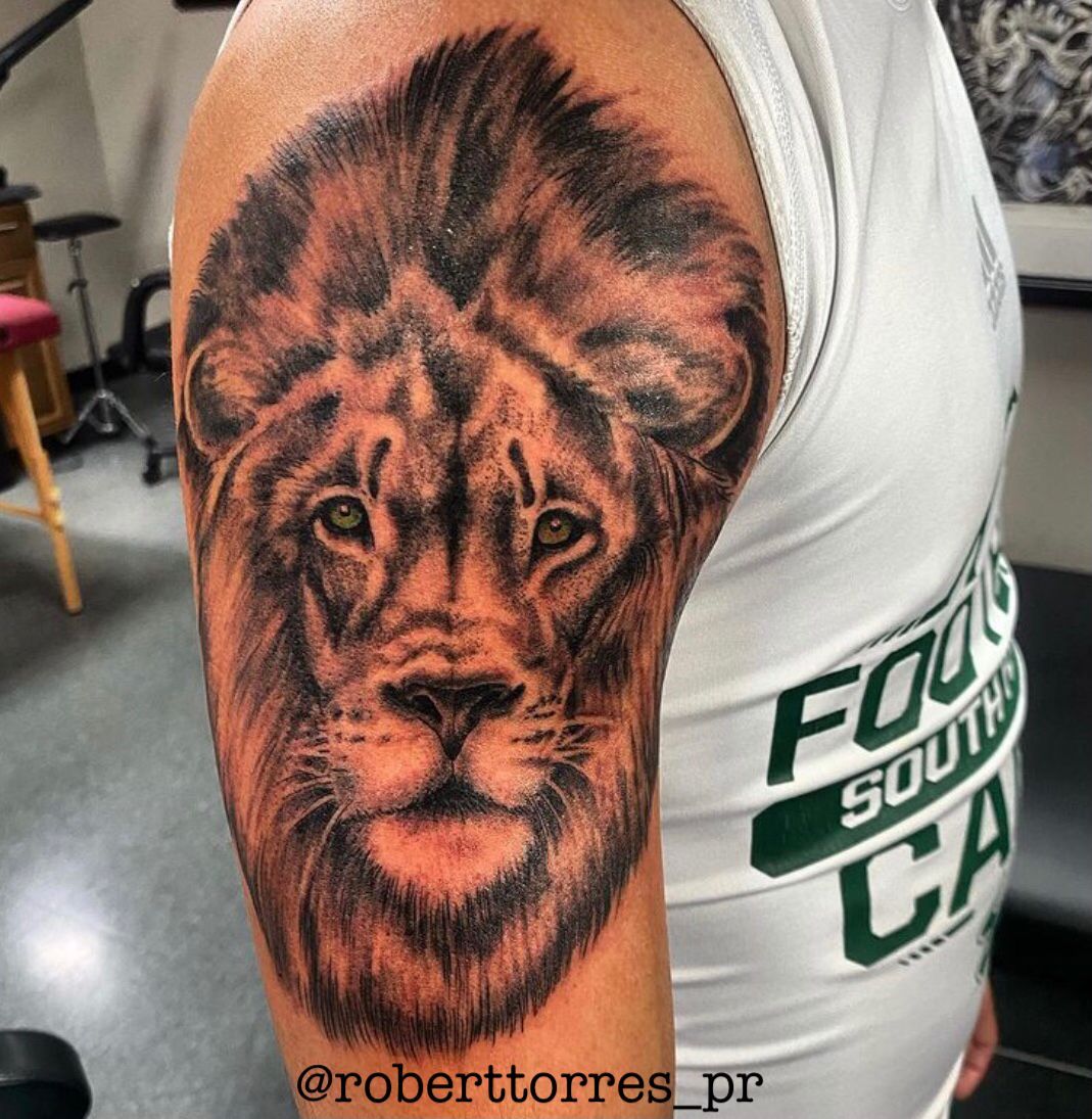 Lion tattoo on a person's upper arm, black and orange shading. The person wears a white t-shirt.