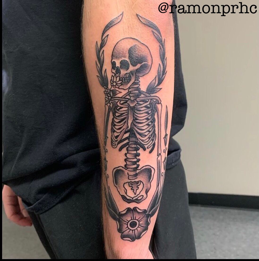 Tattoo of a black and gray skeleton with a floral wreath on an arm.
