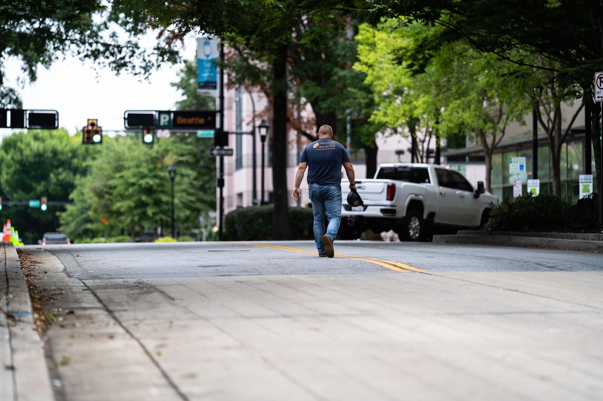 Person walking across a wet city street near parked cars and trees