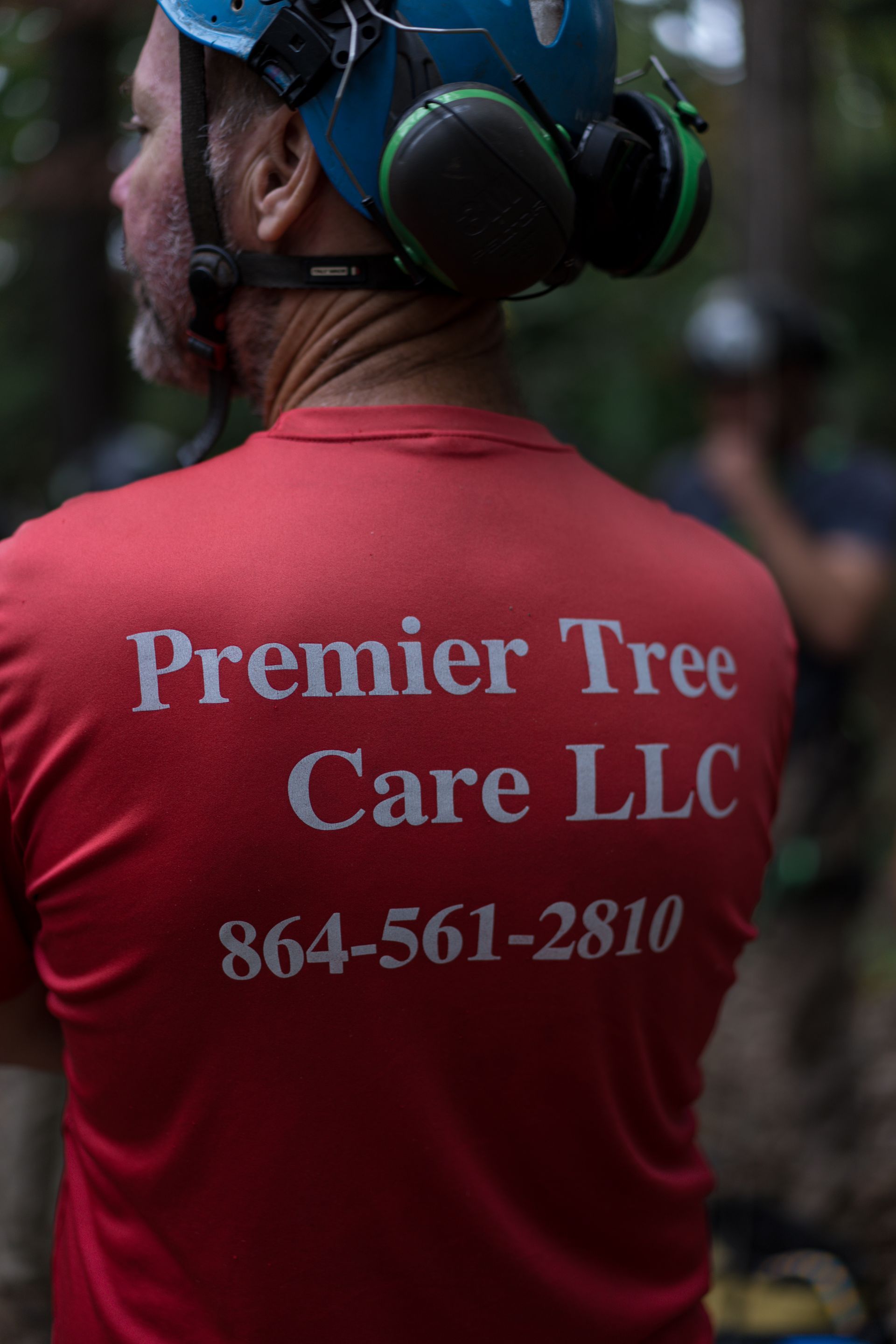 Tree care worker in red shirt with “Premier Tree Care LLC” and phone number on the back