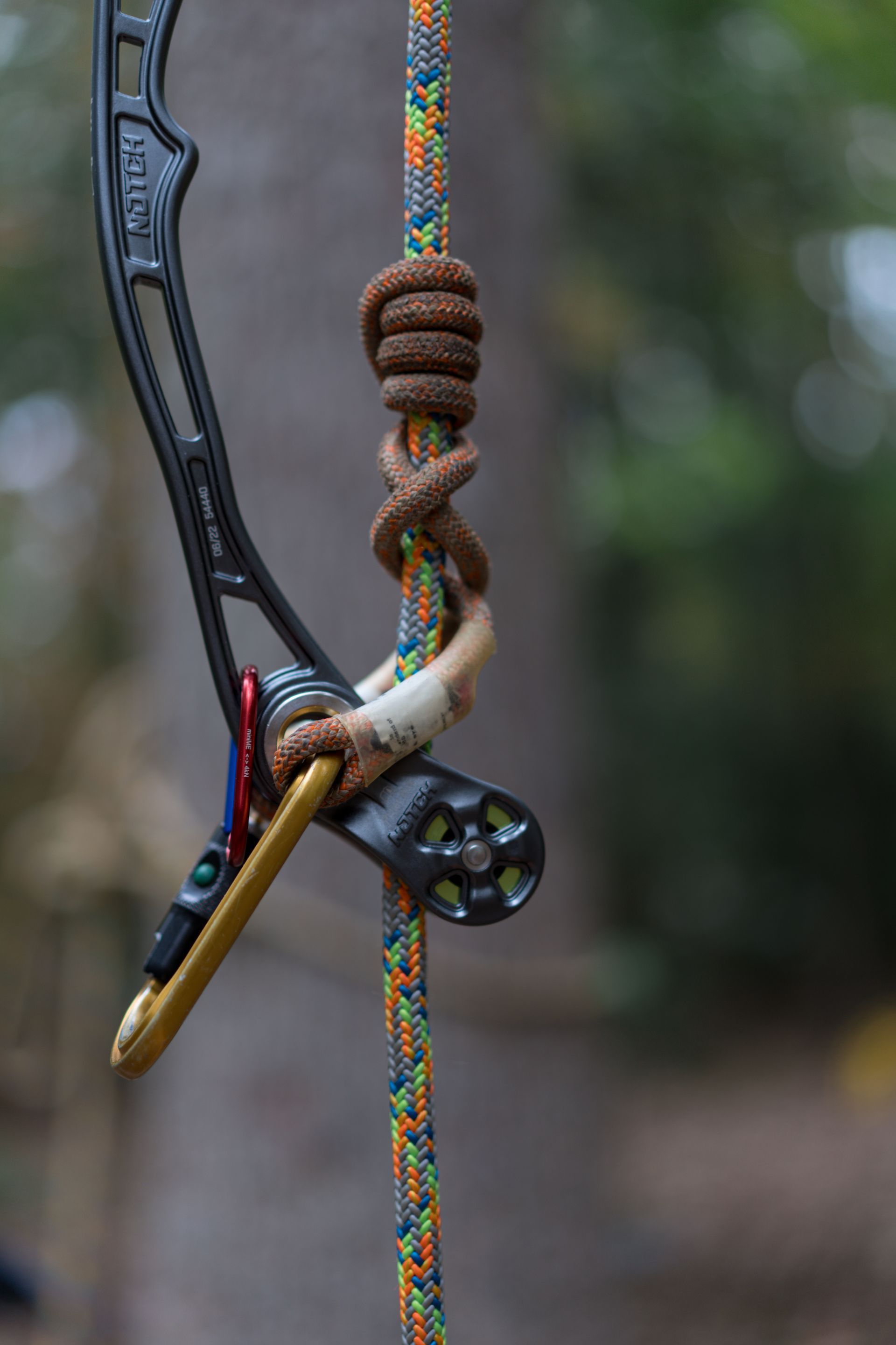 Close-up of a compound bow with a tied rope release and colorful braided string.