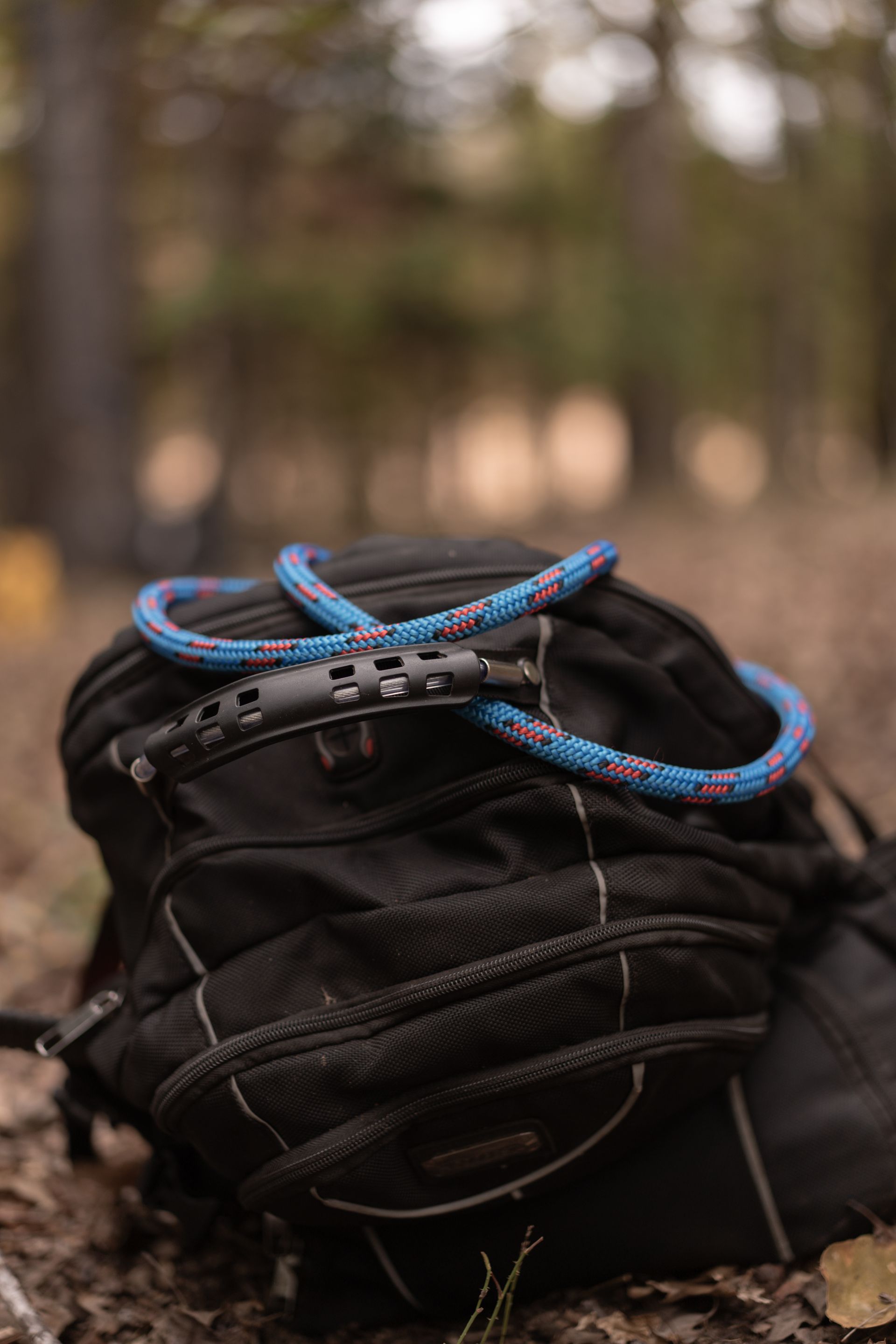 Black hiking backpack with coiled blue and red rope, outdoors on a forest trail