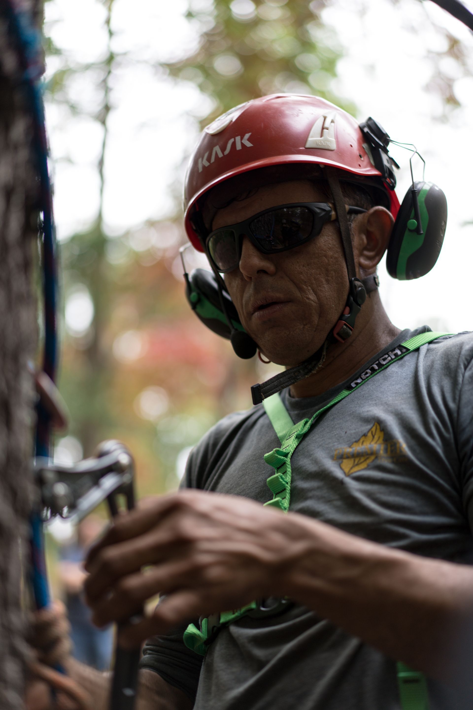 Man in red helmet and sunglasses wearing ear protection and a harness, preparing gear outdoors.