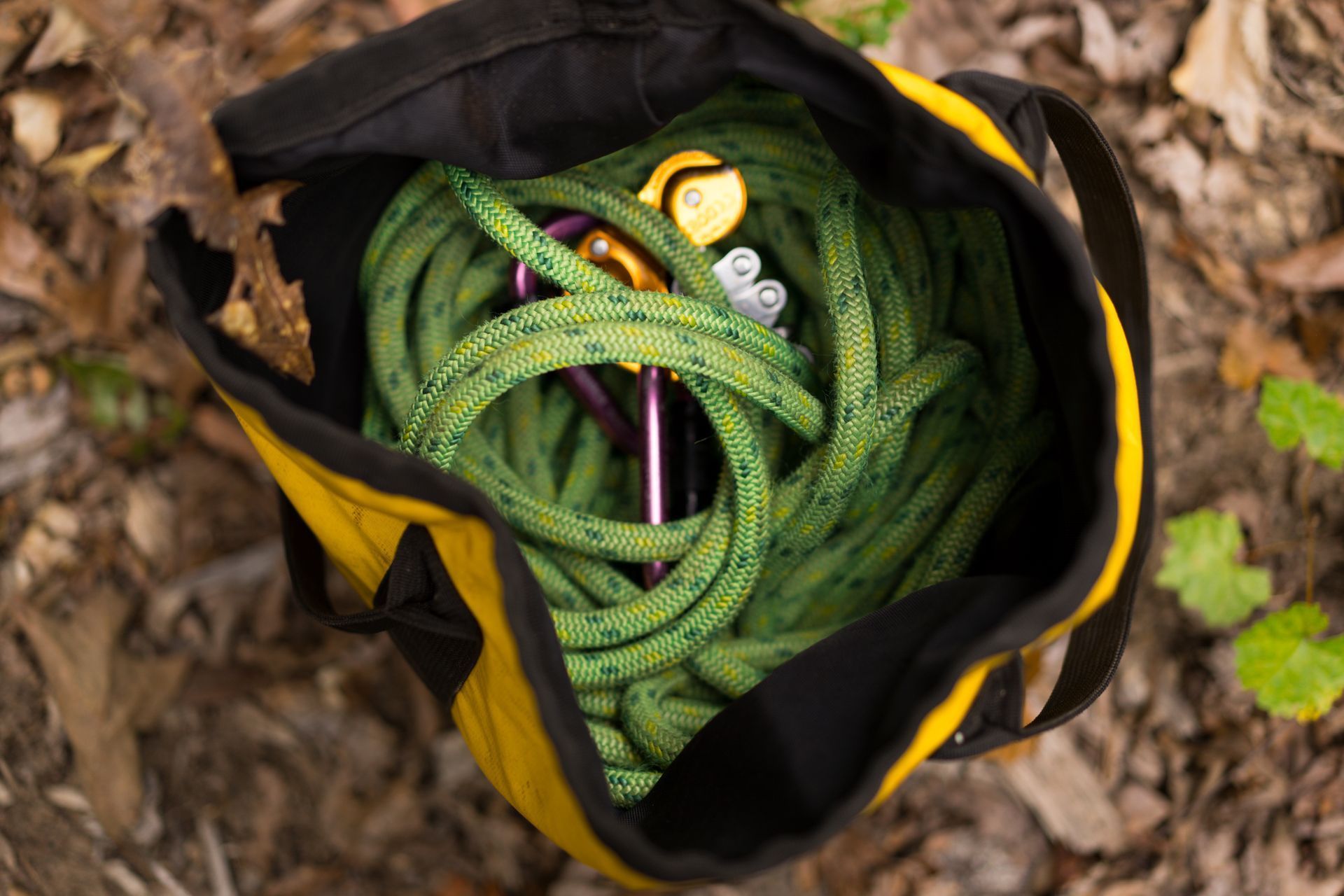 Green climbing rope coiled in a black and yellow gear bag on the ground