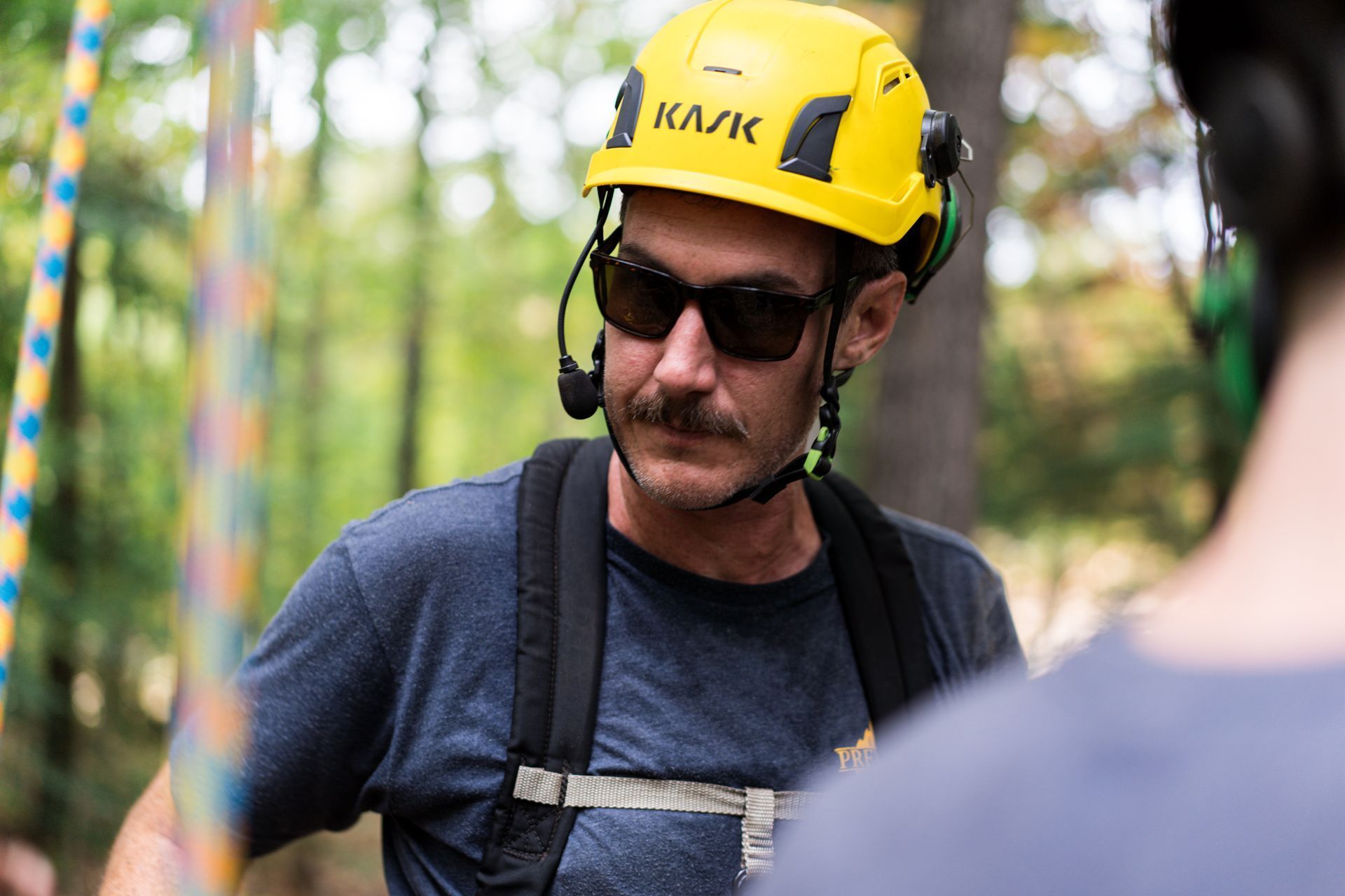 Helmeted worker in harness and sunglasses looking down in an outdoor setting