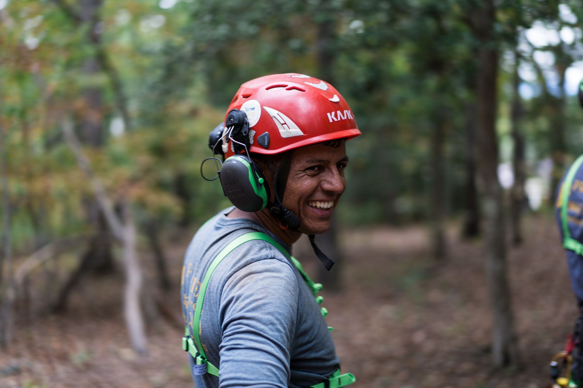 Man in red helmet and green earmuffs smiling in a wooded outdoor setting
