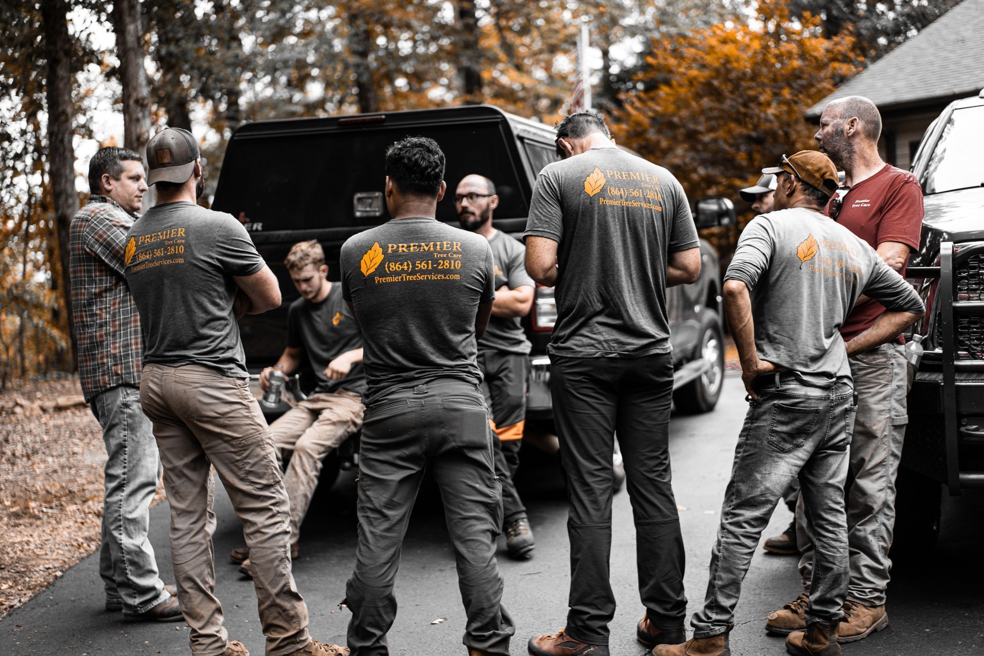 Group of workers in gray shirts standing around a black truck on an autumn street