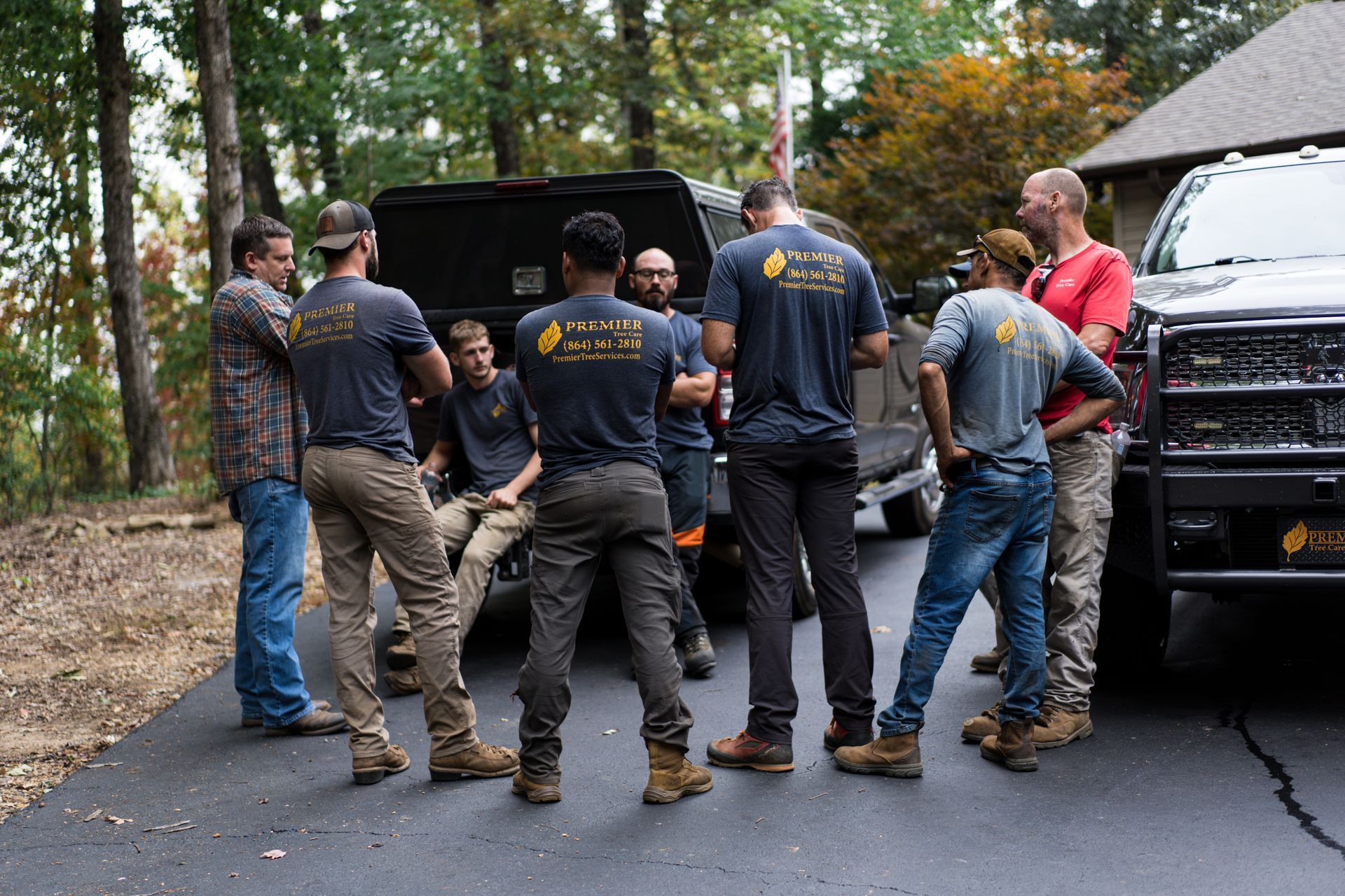 Group of workers in matching shirts standing beside trucks on a wet driveway, facing an open vehicle