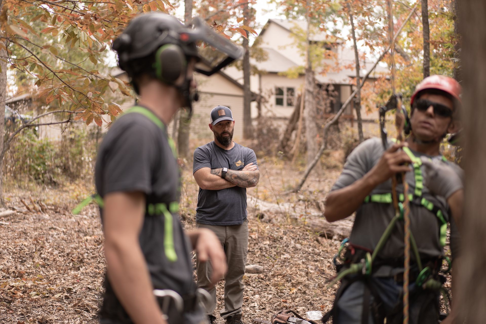 Three hikers with ropes and helmets in a wooded outdoor area, one holding gear in the foreground.