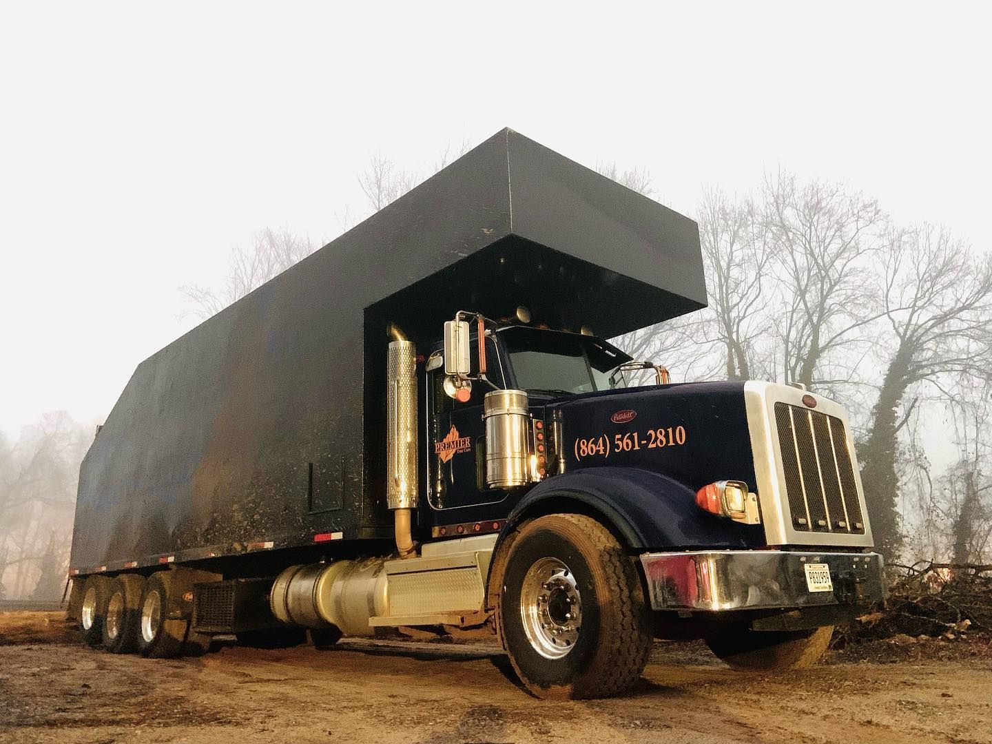 Black semi truck hauling a large black trailer on a foggy roadside