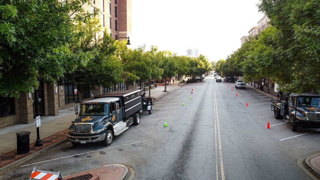 Tree-lined city street with parked trucks and traffic cones on a quiet roadway