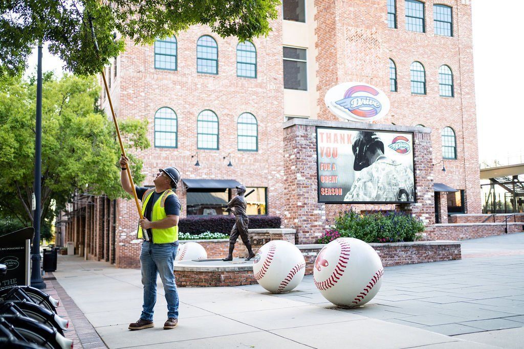 Person in a safety vest photographing large baseballs in a plaza near a brick building.