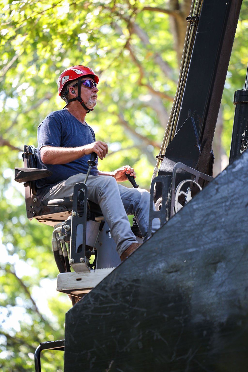 Worker in red helmet operating a boom lift beside a large black structure outdoors.