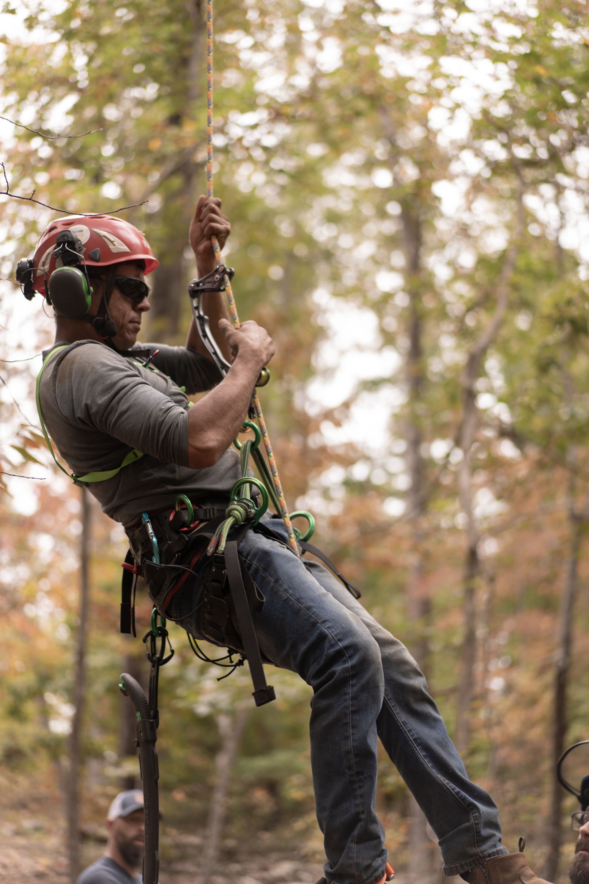Rock climber in a red helmet rappelling down a rope in a forest.