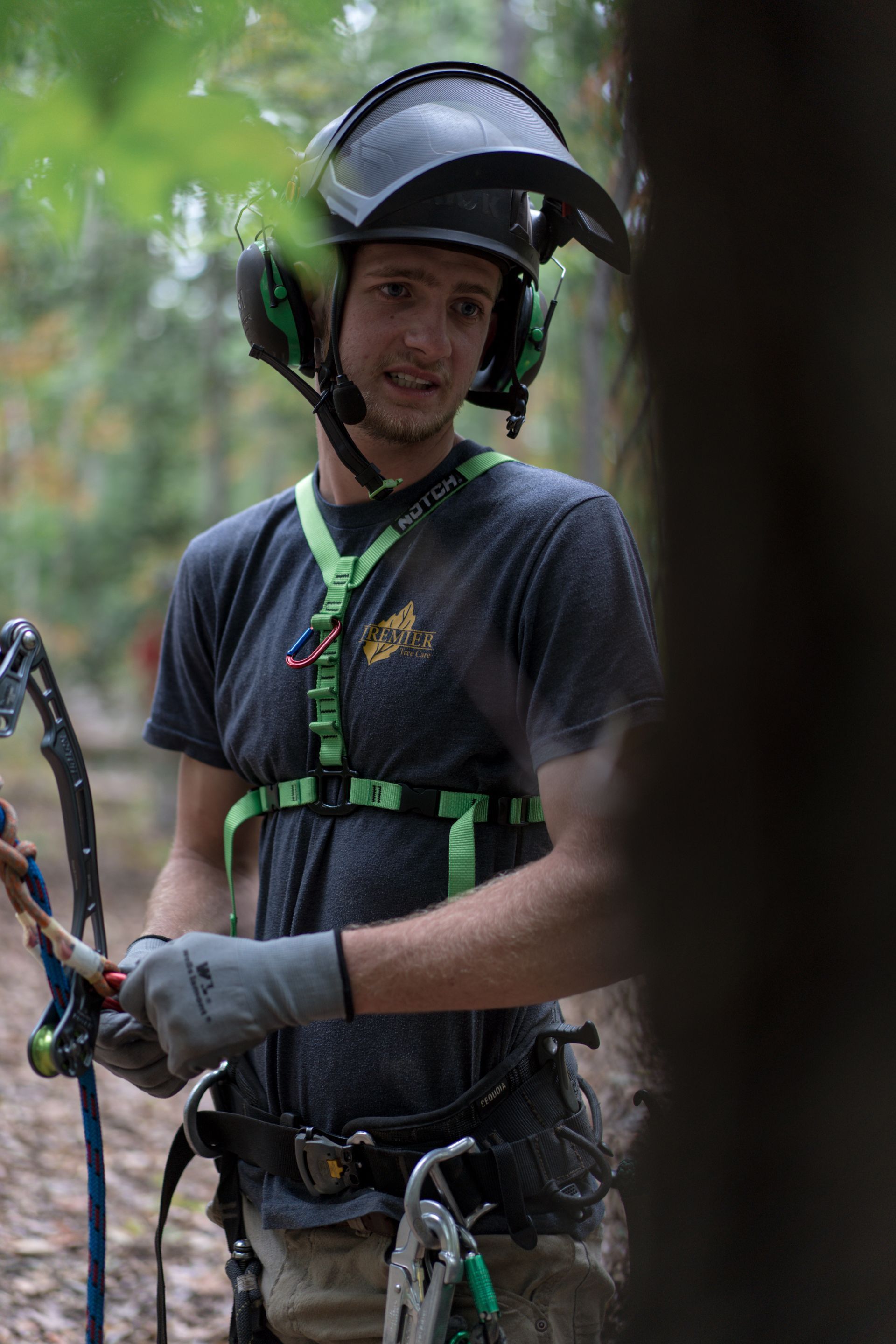 Person in a helmet and safety harness holding a rope in a forested area