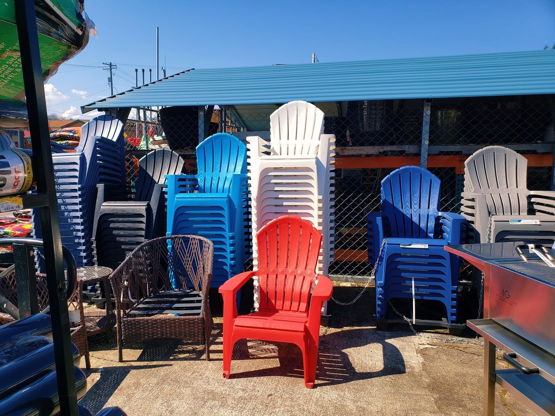 Stacks of colorful plastic chairs, including red, blue, white, and gray, outside in front of a blue roof.