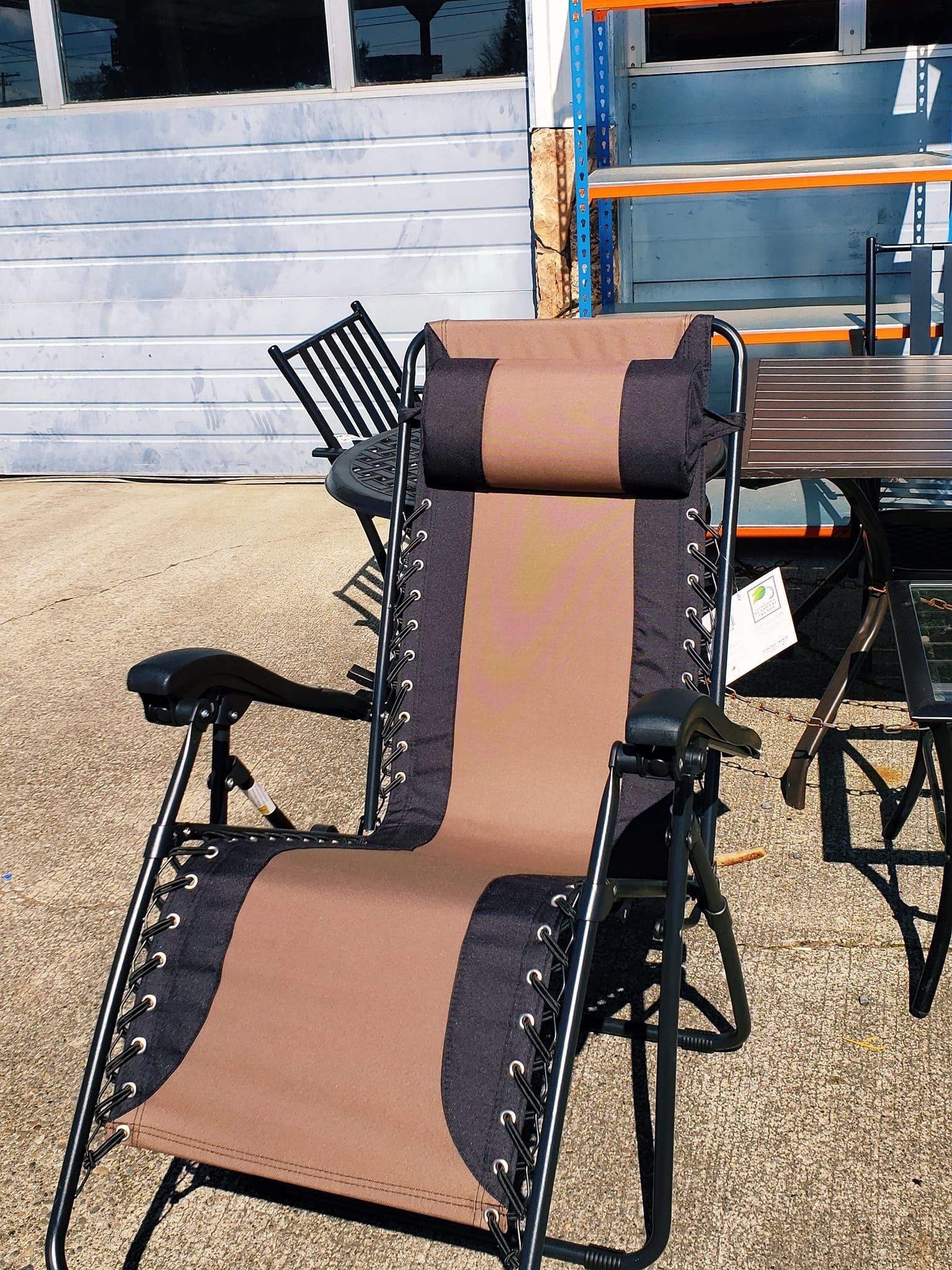 Brown and black zero gravity chair on grass, in front of a metal rack.