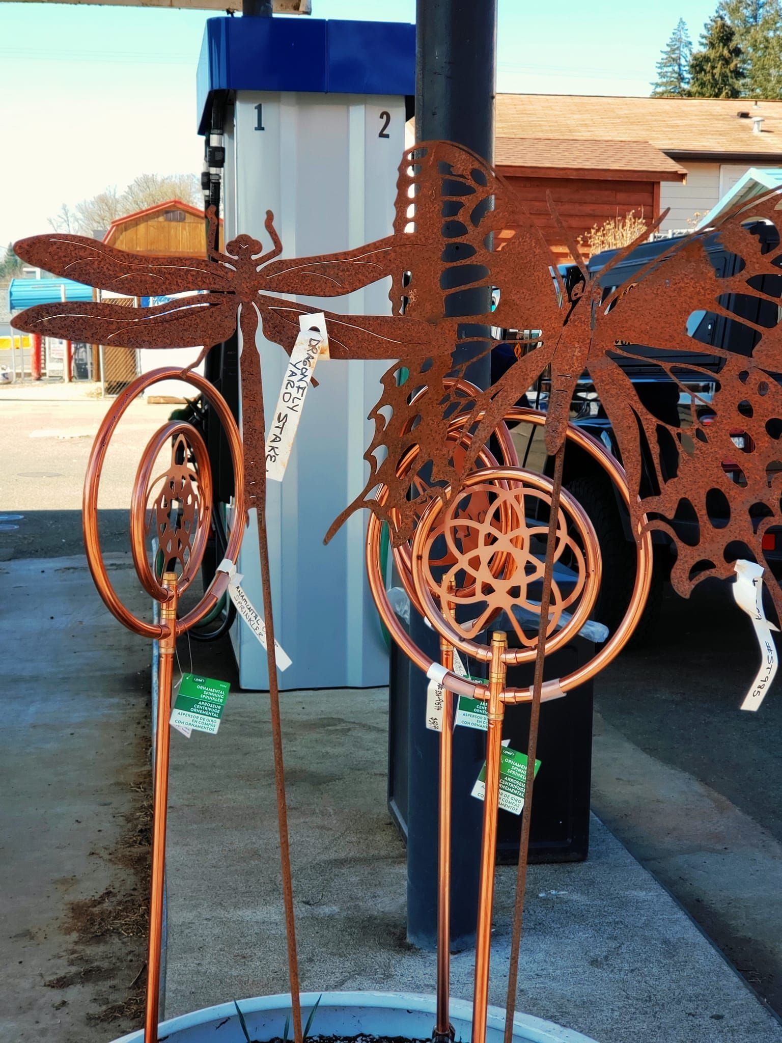 Metal dragonfly and butterfly yard art on display, with price tags, near gas pump.