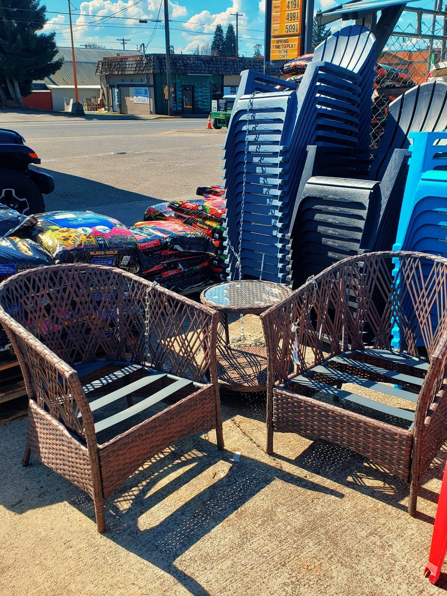 Two wicker patio chairs with cushions and a small table, alongside stacked blue chairs and other outdoor items.