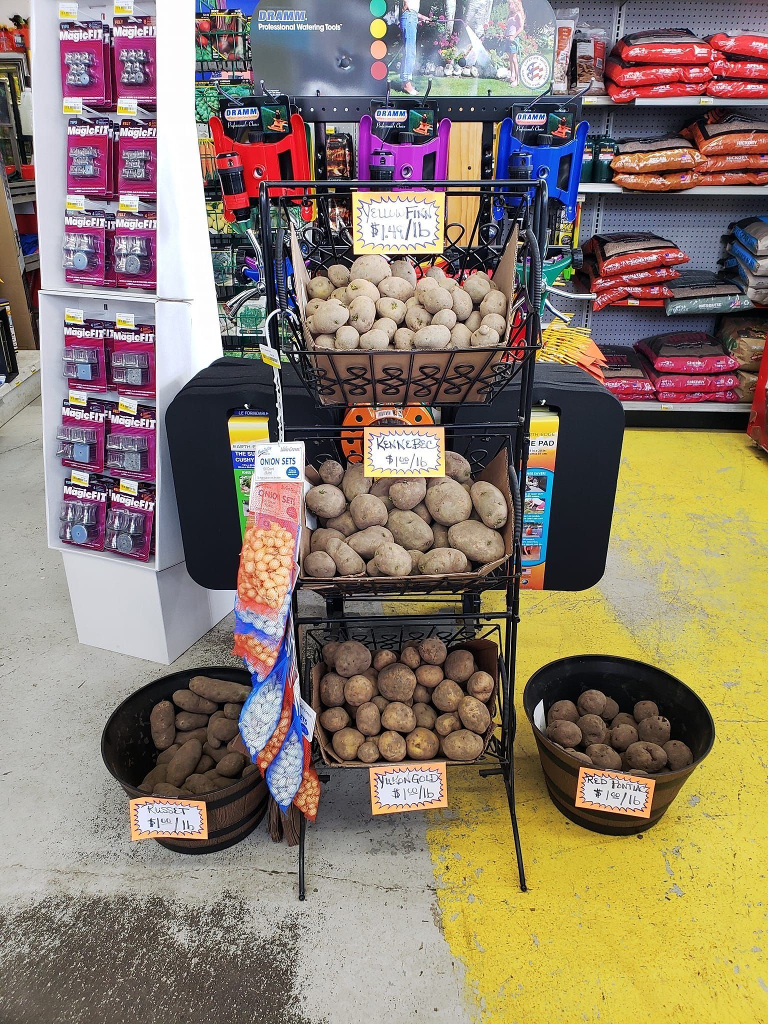Potato display in a store, three-tiered rack with baskets holding different varieties. Baskets on the floor.
