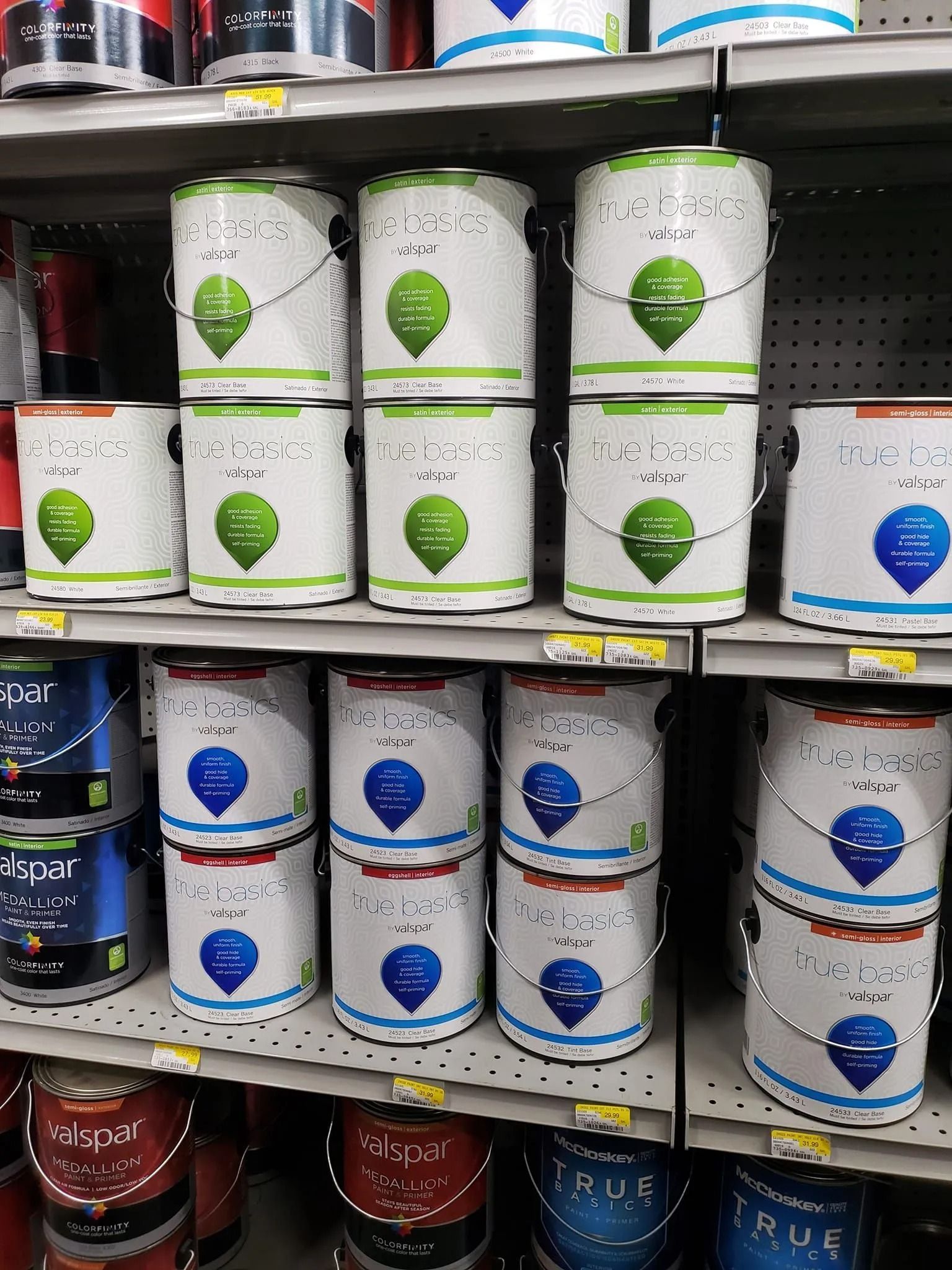 Paint cans stacked on store shelves; various colors, labels, and sizes.
