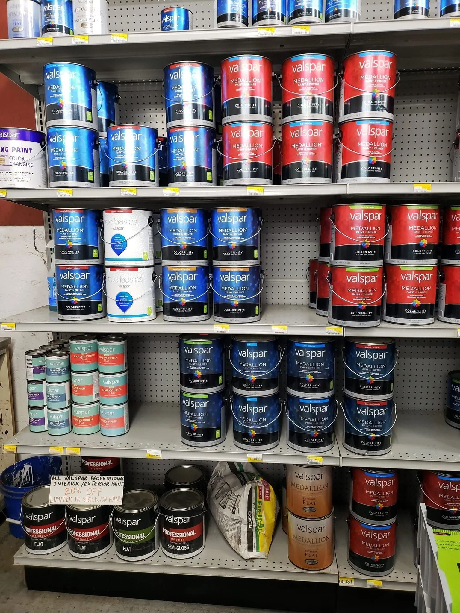 Paint cans stacked on store shelves. Various colors: blue, red, white, black, and orange.