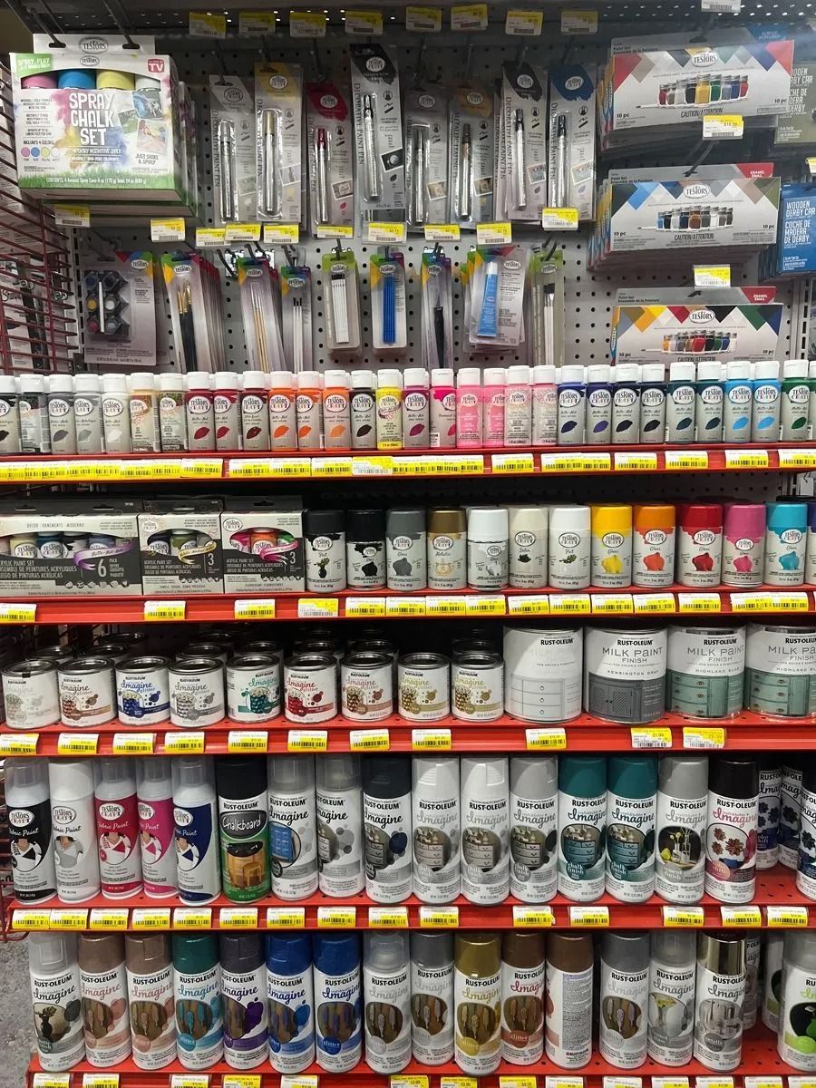 Shelves stocked with various art supplies, including pens, paint bottles, and spray paint cans, in a store setting.