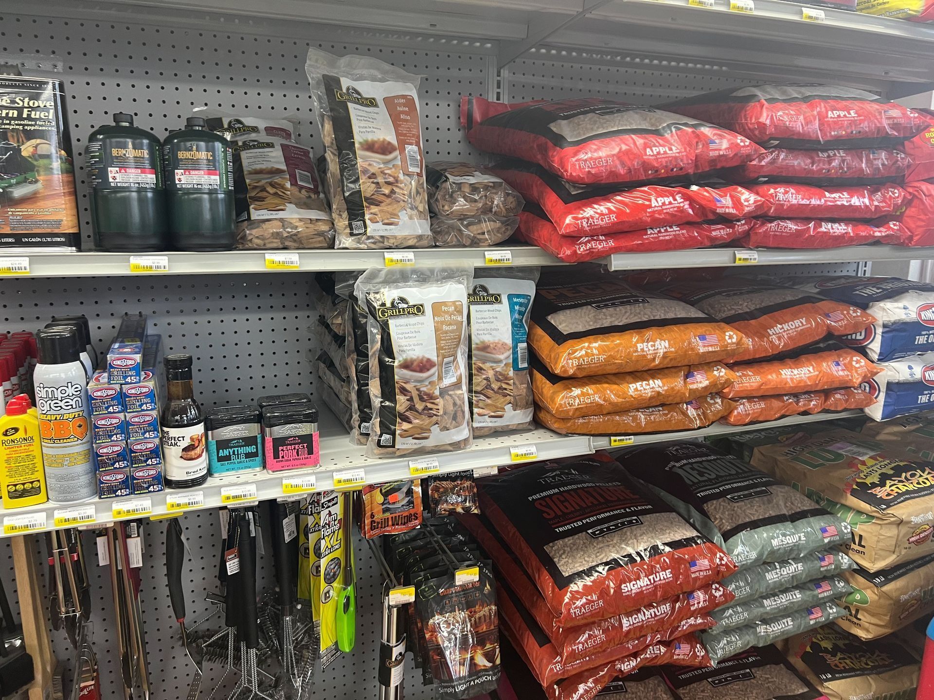 Shelves stocked with propane tanks, grilling wood chips, and bags of wood pellets in a store.
