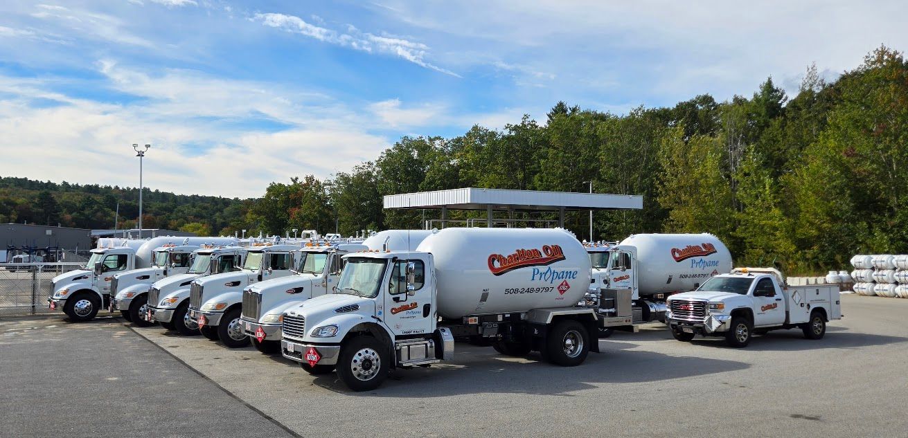 A fleet of white propane trucks parked in a lot, with a canopy overhead and trees in the background.