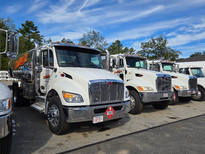 White fuel trucks parked in a lot under a blue sky.