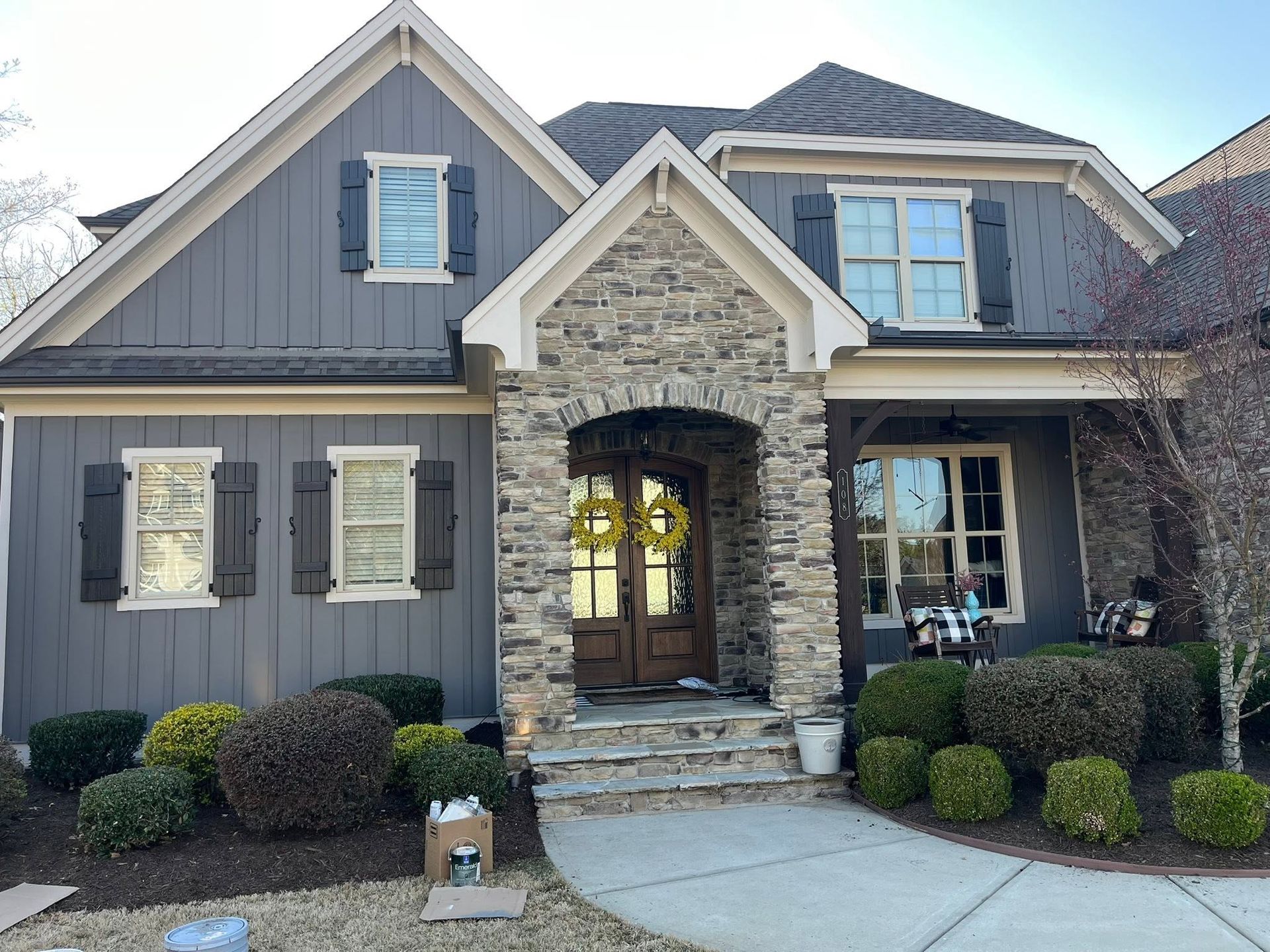 Gray suburban house with stone entry, blue shutters, and a front porch with plants