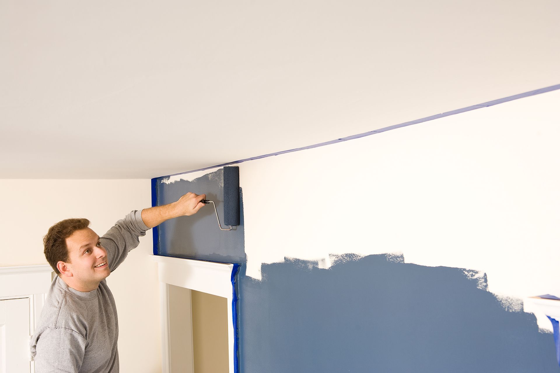 Man painting a wall white and blue with a brush near the ceiling