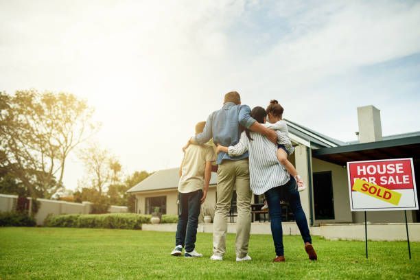 Family standing outside a house for sale, with a red sold sign on the lawn.
