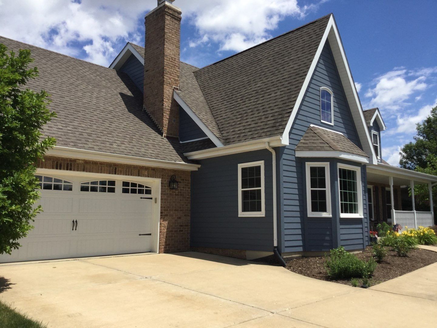 Blue house with a steep roof, white-trim garage, and brick chimney on a sunny day