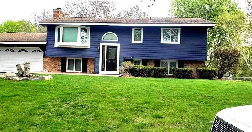 Blue-sided house with white trim, bay window, and a green lawn.