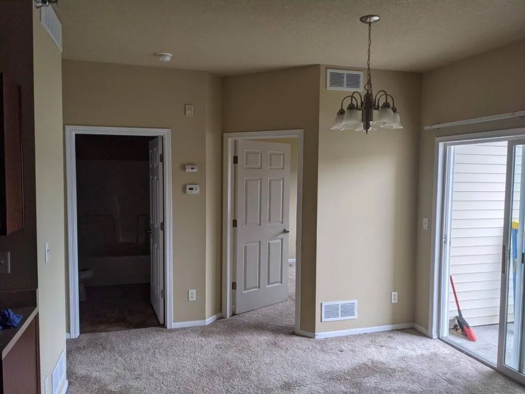 Beige room with doorways to bathroom and hallway, sliding door to patio, brown carpet.