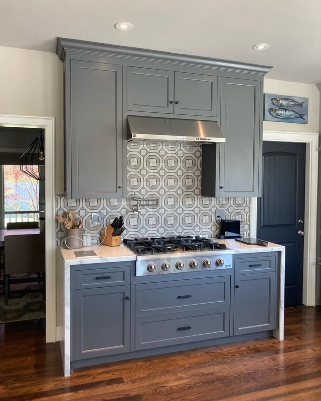 Gray kitchen island with stove, cabinets, and tiled backsplash. Wooden floor.